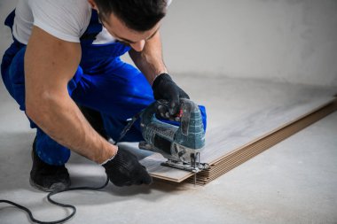 Sakallı işçi, tahta bir tahtayı yapbozla kesiyor.