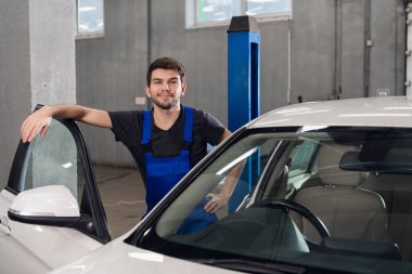 Gülümseyen adam beyaz bir arabanın yanında duruyor.