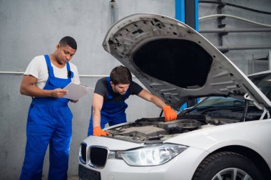 Atölye çalışanları bir arabayı tamir edip rapor yazıyorlar.