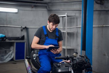 Tamirci motosiklette oturuyor ve tablet kullanıyor.