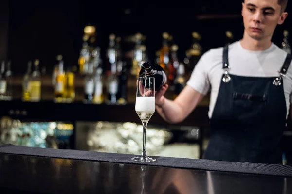 Młody barman nalewa szampana do szklanki z butelki na barze — Zdjęcie stockowe