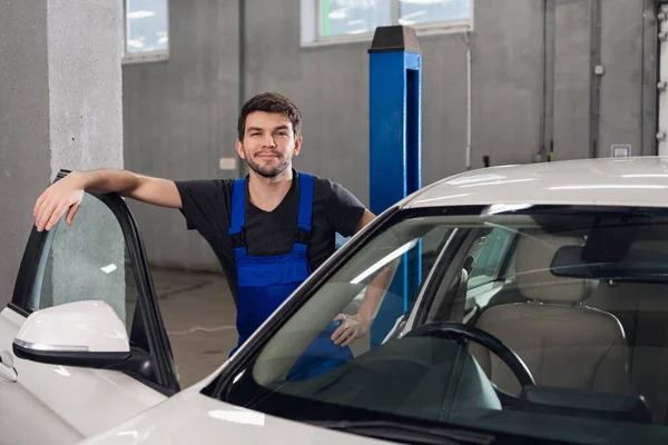 Gülümseyen adam beyaz bir arabanın yanında duruyor.