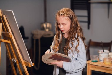 Bir sanat okulu öğrencisi bir atölyede tuval çizimi için paletin renklerini karıştırıyor..