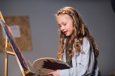 Bir sanat okulu öğrencisi bir atölyede tuval çizimi için paletin renklerini karıştırıyor..
