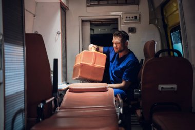 Sağlık görevlisi ambulans arabasında oturuyor ve tıbbi aletlerini topluyor.