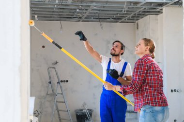 Bir işçi bir kadına duvarı nasıl doğru boyayacağını söyler.