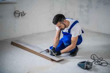 Sakallı genel işçi, tahta bir tahtayı yapbozla kesiyor.