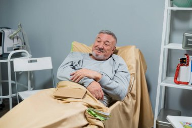 Hastane yatağında mutlu yaşlı bir adam, mutlu görünüyor.