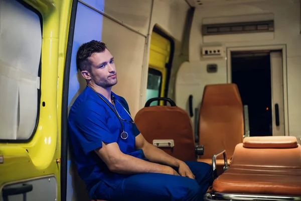 Paramédico cansado con uniforme azul sentado en un coche ambulancia —  Fotos de Stock