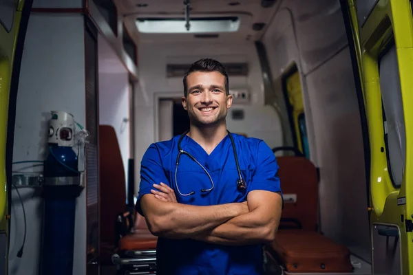 Ένα πορτραίτο ενός νεαρού ειδικευόμενου που στεκόταν μπροστά από ένα ασθενοφόρο με τα χέρια του διπλωμένα και χαμογελαστά. — Φωτογραφία Αρχείου