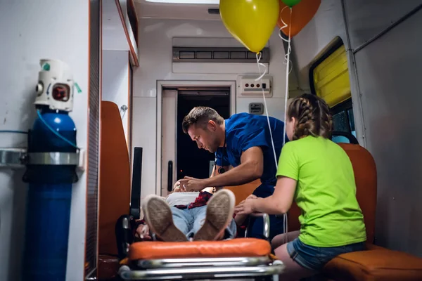 Мать без сознания лежит на носилках в машине скорой помощи, парамедик оказывает ей первую помощь — стоковое фото