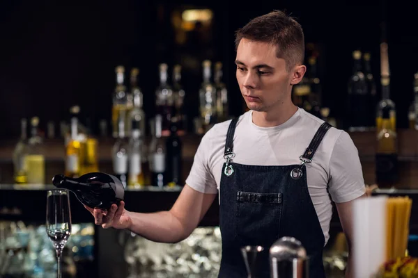 Молодий чоловік бармен наповнює келих шампанського в барі в нічному клубі — стокове фото