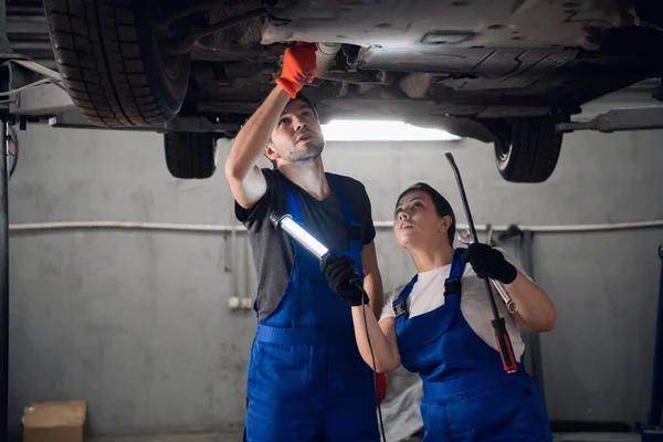 Two mechanics repair a car and use a flashlight