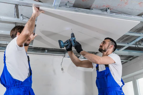 Un uomo e il suo collega fissare una piastra di cartongesso al soffitto — Foto Stock