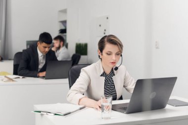Bir çağrı merkezi çalışanı, büyük bir finans şirketinin ofisindeki bir masada katı bir ofis kıyafet yönetmeliğiyle oturur..