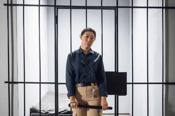 A young prison guard poses in front of prison bars in uniform. In a maximum security prison