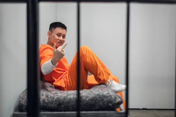 Šílený člen čínského mafiánského gangu sedí v cele a ukazuje kameře obscénní gesto. — Stock fotografie
