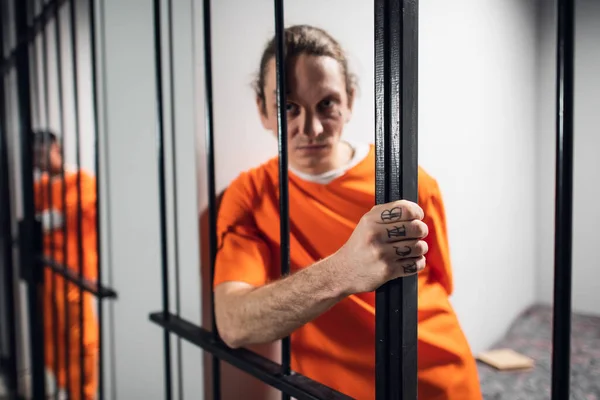 Psychological portrait of an evil and wild prisoner through the bars of a prison cell. A strong look and emotions. — Stock Photo, Image