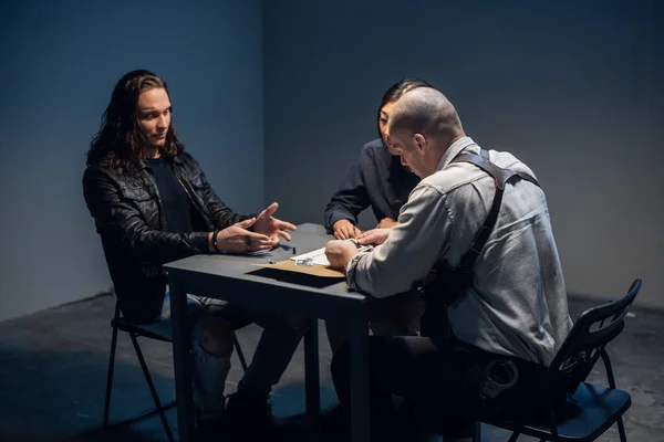 In the police stations interrogation room, good and bad cops are questioning a theft suspect in a leather jacket.