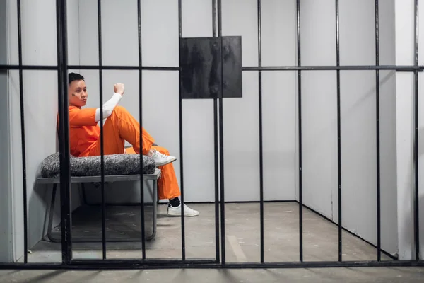 Solitary cell with a criminal in an orange robe in an asian prison. Copy space. Sad emotions of a young guy. — Stock Photo, Image