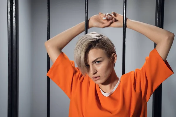 Portrait of a beautiful blonde with short hair on the background of prison bars — Stock Photo, Image