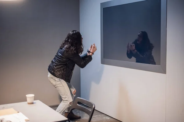 A white man with tattoos on his face tries to break the Gesell mirror in the police station interview room, because he is innocent of the crime he is accused of