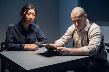 An experienced police officer and his young assistant sit at the table and sort out the case clipart