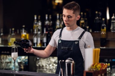 Genç bir erkek barmen bir gece kulübünde bir bardak şampanya dolduruyor.