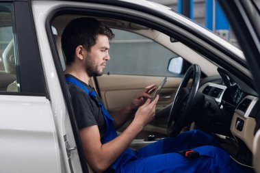 Tamirci arabada oturuyor ve akıllı telefon kullanıyor.