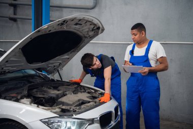 Tamirciler araba motoru tamir eder ve rapor yazar.