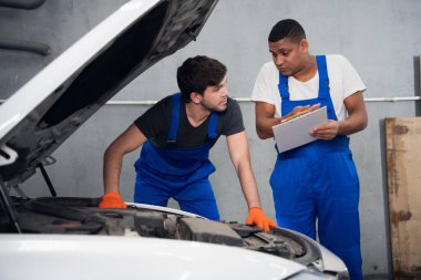 Tamirci genç bir adama araba tamir etmeyi öğretiyor.