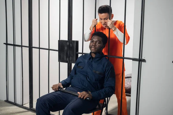 Чорний в'язничний охоронець сидить перед клітками з небезпечними злочинцями на стільці з кажаном . — стокове фото