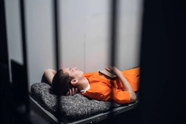 Um prisioneiro perigoso em uma cela descansa e dorme em uma cela solitária em um beliche em um manto laranja. — Fotografia de Stock