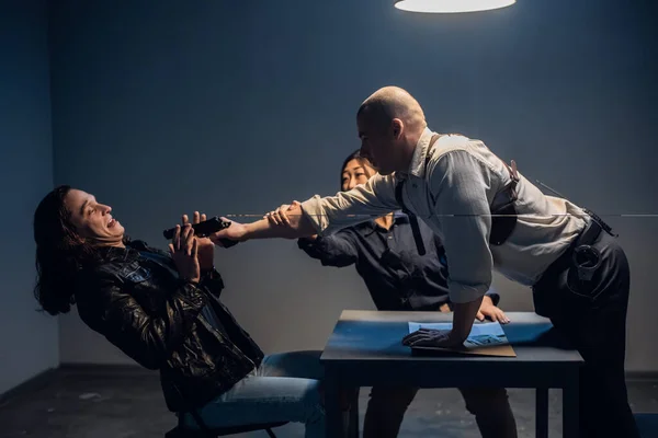 Violence by a police officer against a suspect in an interrogation room. An officer threatens a man with a weapon in the presence of a witness. — Stock Photo, Image