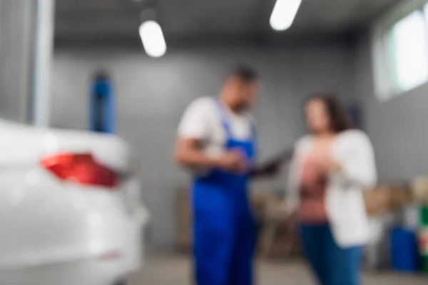 Blurred background of repairer tells customer about car repair. — Stock Photo, Image