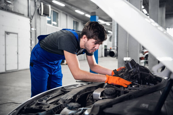 Mechanic in gloves fixing car with open hood