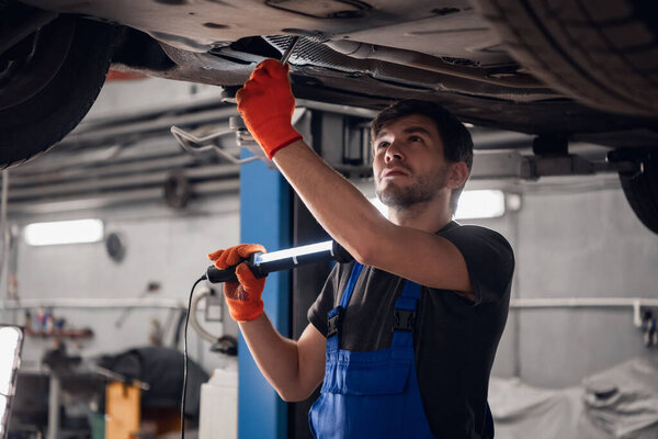 Mechanic checks the car bottom and shines a torch