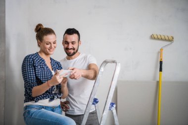 Bir adam ve genç bir kız, bir apartman dairesinde yenilenen akıllı telefondan çekilmiş bir fotoğrafa bakıyorlar.