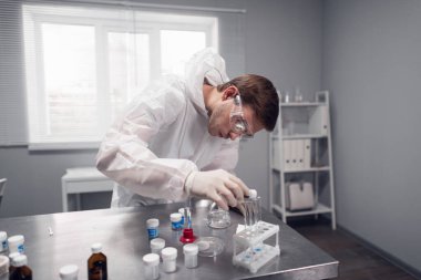 Bilim adamı laboratuardaki test tüplerine bazı kimyasal ürünler döküyor.