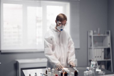 Arka plan bulanık. Kimya laboratuvarında çalışan genç bir bilim adamı ısıtma maddeleri üzerinde deney yapıyor.