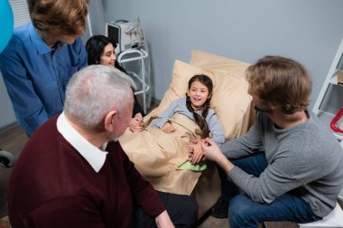 Küçük bir kızın yatağını çevreleyen bir aile, bir kazadan sonra hastanede kalıyor, ziyarete geldiler.
