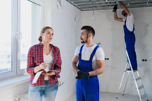 A female customer talks to a builder in uniform and takes notes in a notebook — Stock Photo, Image