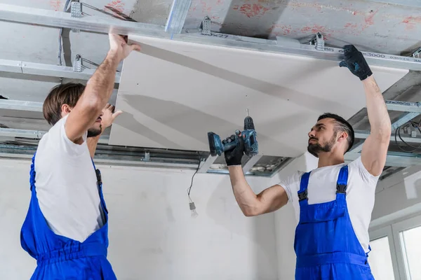 A worker and his colleague fix a plasterboard plate to the ceiling — Stock Photo, Image