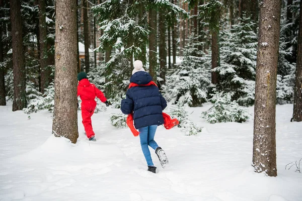 Menina e menino em roupas de inverno correndo na floresta de neve de inverno, visão traseira — Fotografia de Stock