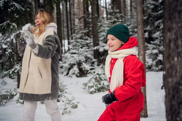 В зимнем лесу на прогулке мама с сыном бросают снег, веселые семейные игры — стоковое фото