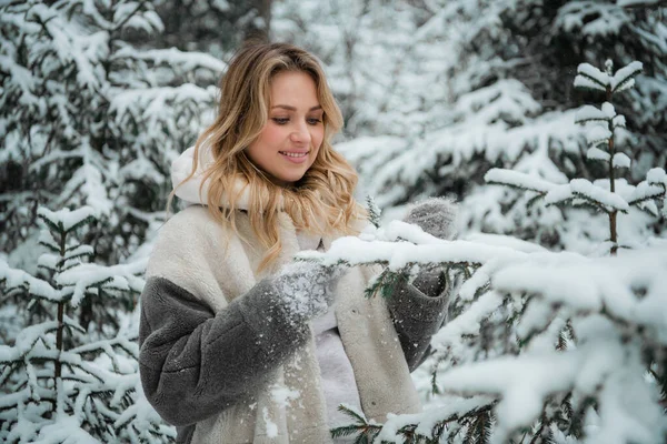 Una bella giovane moglie passeggia nel cortile della sua casa di campagna in una foresta di abeti rossi invernali e gode della natura e della tranquillità.. — Foto Stock