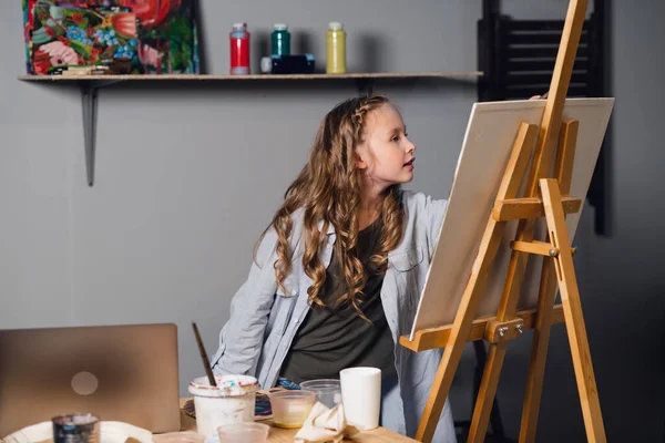 cute girl artist draws her oil painting from a reference from a laptop.