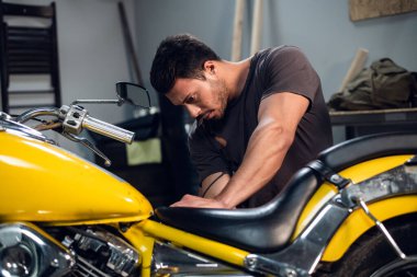 Otomobil tamirhanesinde motosiklet ayarlayan genç bir tamirci. Hobiler ve iş etkinlikleri.