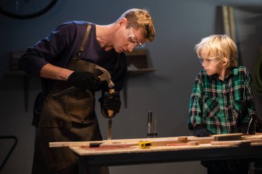 Genç bir baba, garajda oğluna marangozluğu öğretiyor..