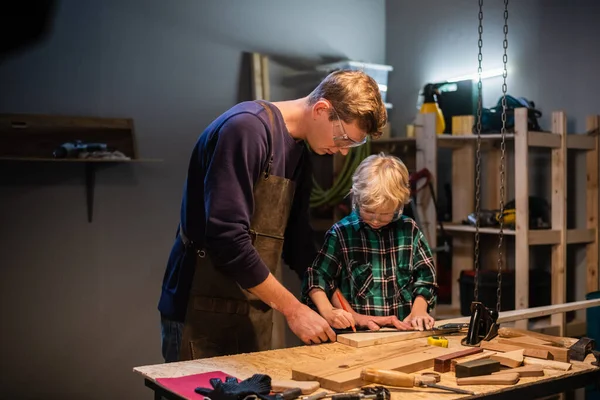 an experienced carpenter and his young apprentice make wood crafts in their workshop.